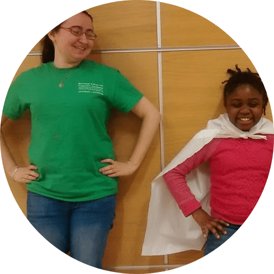 Carly stands next to a young student wearing a superhero cape.